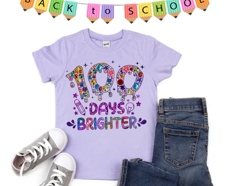 Op de afbeelding: Paars T-shirt met een glinsterend ontwerp met de tekst "100 dagen stralender" met een potlood en een gloeilamp.