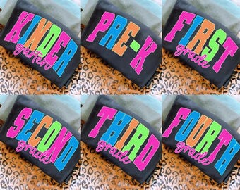 May include: Black t-shirts with vibrant text indicating school grades: Kindergarten, Pre-K, First Grade, Second Grade, Third Grade, and Fourth Grade. The text is in pink, orange, green, and blue.