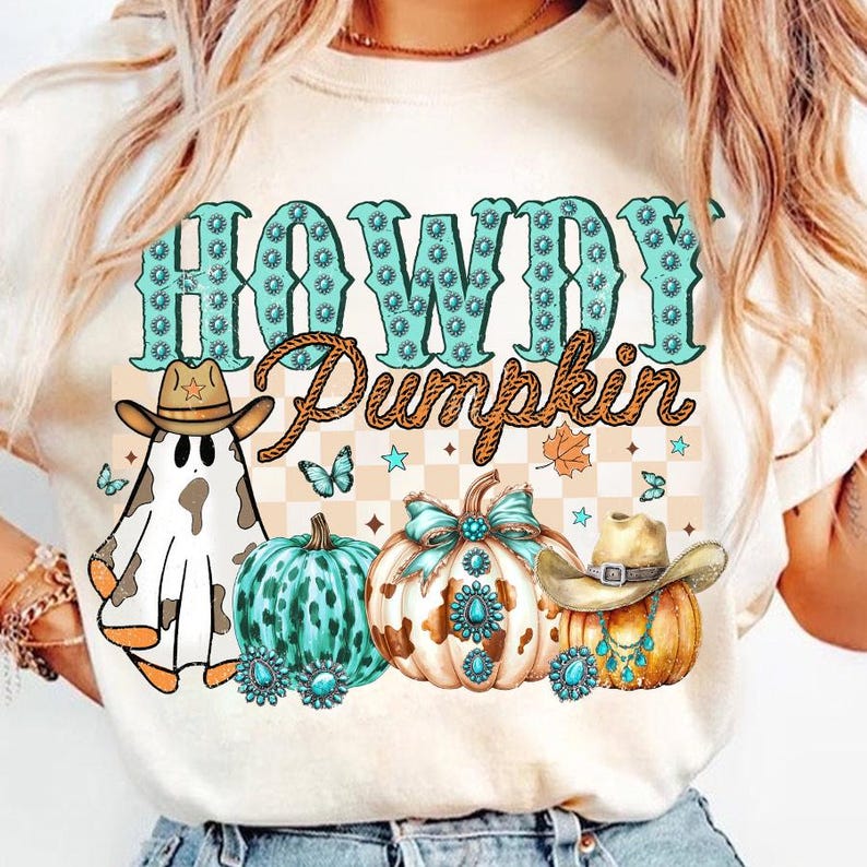 May include: A white t-shirt with the text "Howdy Pumpkin" in turquoise blue with rhinestones. The design also includes a ghost wearing a cowboy hat, a turquoise and white pumpkin, and a pumpkin with a cowboy hat and turquoise jewelry.