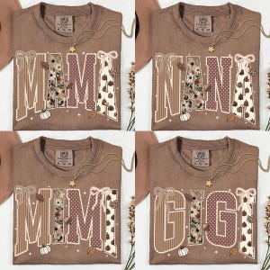 Peut inclure: Quatre t-shirts marron avec de grandes lettres majuscules formant MAMA, NANA, MIMI et GIGI. Chaque lettre est orn&eacute;e de rayures, de pois et d'imprim&eacute;s floraux ou de citrouilles, agr&eacute;ment&eacute;e de n&oelig;uds blancs, de petites &eacute;toiles et de feuilles.