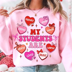 May include: Pink sweatshirt with the text "My Students Are" surrounded by hearts with words like "Friendly", "Kind", "Strong", "Enough", "Creative", "Loved", "Brave", and "Worthy".