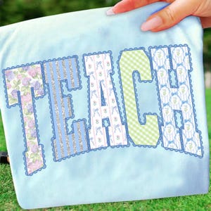 May include: Light blue t-shirt with the word "TEACH" in decorative letters. The letters feature floral, striped, and gingham patterns, outlined with a scalloped border. The shirt is held by a hand.