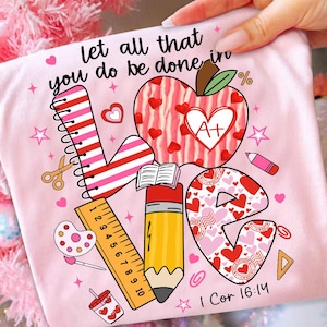 May include: Pink t-shirt with the word "LOVE" in a colorful design. The design includes an apple with a heart, a pencil, a ruler, and the text "let all that you do be done in" and "I Cor 16:14".