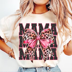 May include: White t-shirt with a graphic print of the word "MAMA" repeated three times with a large pink and brown leopard print bow in the center.
