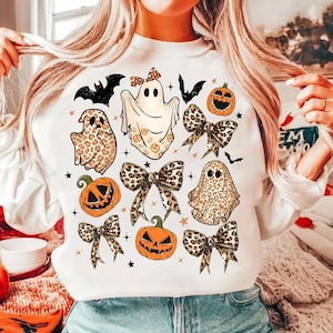 May include: White sweatshirt with a Halloween theme featuring ghosts, pumpkins, bats, and leopard print bows.
