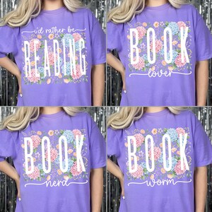 May include: Four lavender t-shirts with floral designs and white text. One shirt says "I'd rather be READING", another says "BOOK lover", a third says "BOOK nerd", and the last says "BOOK worm". The shirts have short sleeves.