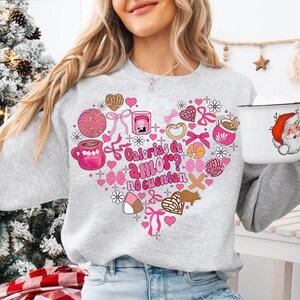 May include: A gray sweatshirt with a pink heart design featuring various Mexican sweets and the text "Calorias de amor? No cuentan".
