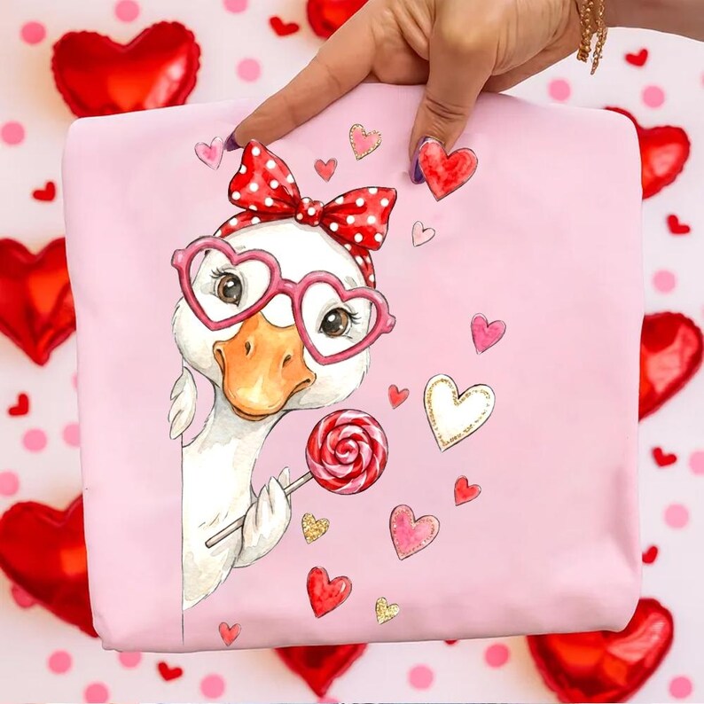 May include: Pink fabric featuring a cartoon goose wearing heart-shaped glasses and a red bow. The goose holds a lollipop and is surrounded by heart illustrations. The background includes red heart-shaped balloons and pink polka dots.