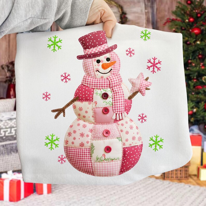 May include: A white cushion cover with a patchwork snowman design. The snowman has a top hat, scarf, and star, with pink and red accents. Green and pink snowflakes are scattered around the snowman.
