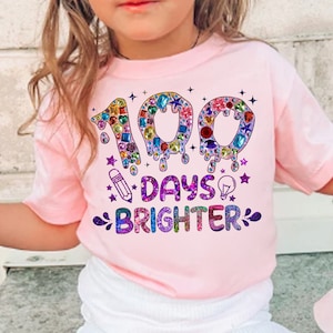 Op de afbeelding: Roze T-shirt met een kleurrijke afbeelding met de tekst "100 dagen stralender". De afbeelding bevat een getal 100 gemaakt van kleurrijke juwelen en een potlood en een gloeilamp.