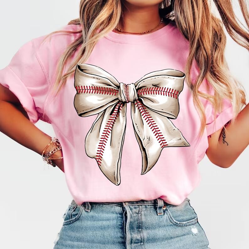 May include: A pink t-shirt with a white baseball-stitched bow on the front.