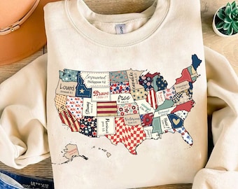 Op de afbeelding: Een beige sweatshirt met een patchwork-ontwerp van de kaart van de Verenigde Staten. Elke staat is in een andere kleur en patroon met inspirerende woorden en bijbelteksten. De woorden omvatten "Loved", "Empowered", "Brave", "Free", "Capable", "Strong", "Precious", "Victorious", "Redeemed", "Bold", en "Important".