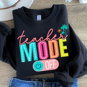 May include: Black sweatshirt with the text "teacher mode off" in colorful letters with a light switch graphic. The text is outlined with white dots and the switch is blue and pink.