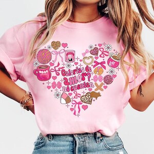 May include: Pink t-shirt with a heart-shaped design featuring various Mexican pastries and the text "Calorias de amor? No cuentan".