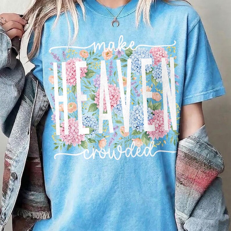 May include: A light blue t-shirt with the words "make HEAVEN crowded" in white. The word "HEAVEN" is in large capital letters, with a floral design of pink, blue, and peach flowers behind it.