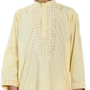 May include: A light yellow long-sleeved shirt with a white embroidered design on the front. The shirt has a mandarin collar and a single button closure.