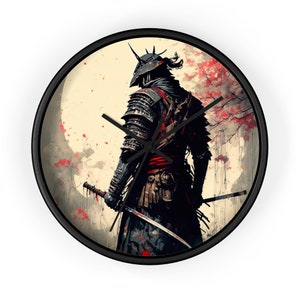 Op de afbeelding: Ronde wandklok met een zwart frame. De wijzerplaat toont een samoerai-krijger in harnas, met een katana. De achtergrond is crèmekleurig met rode bloemaccenten en een volle maan.