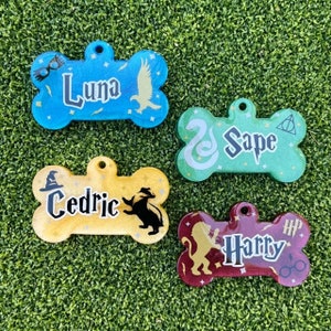 May include: Four colorful bone-shaped dog tags with Harry Potter themed designs. The tags are blue, green, yellow, and red with glitter accents. The names Luna, Snape, Cedric, and Harry are written on the tags.