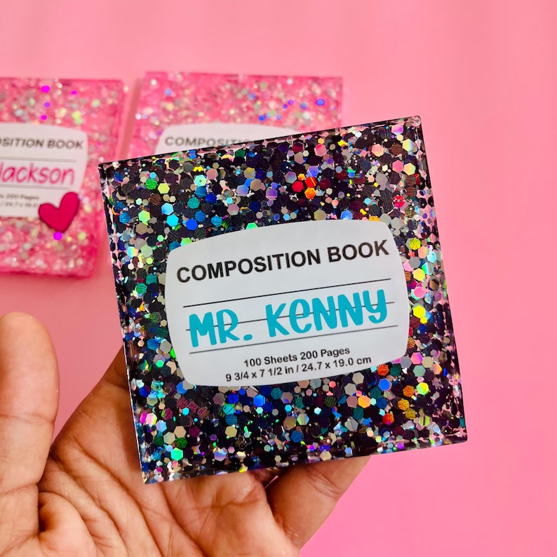 Puede incluir: Un cuaderno de composici&oacute;n negro y plateado con purpurina con una etiqueta blanca que dice "COMPOSITION BOOK MR. KENNY 100 Sheets 200 Pages 9 3/4 x 7 1/2 in/24.7 x 19.0 cm".