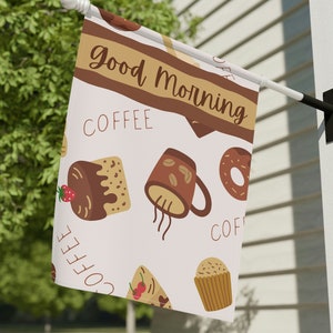 May include: A white flag with a brown and white pattern of coffee cups, donuts, and pastries. The text "Good Morning" is written in a brown banner across the top of the flag. The text "Coffee" is repeated in brown letters throughout the flag.