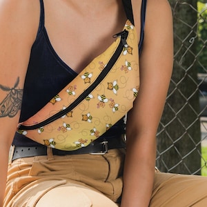 May include: A woman wearing a black tank top and brown cargo pants with a yellow and orange fanny pack with a bee pattern. The fanny pack has a black zipper and a black strap.
