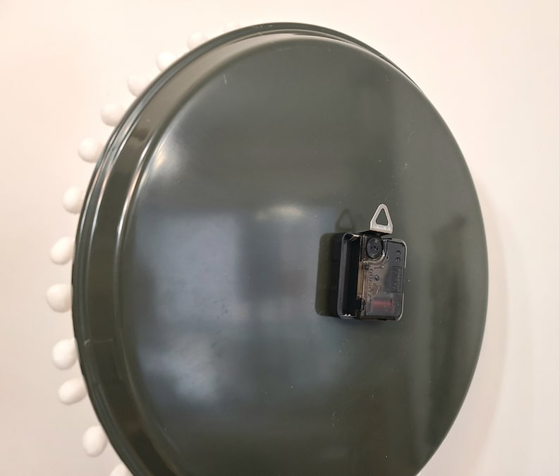 Peut inclure: L'arri&egrave;re d'une horloge ronde vert fonc&eacute; avec une bordure blanche et des points blancs autour du bord. L'horloge a un m&eacute;canisme d'horloge noir avec un crochet argent&eacute;.