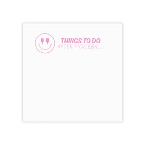 Op de afbeelding: Een wit notitieblok met een roze smiley met twee roze paddle rackets voor ogen. De tekst "THINGS TO DO AFTER PICKLEBALL" staat in roze onder de smiley.