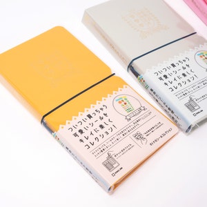 May include: Two yellow and white notebooks with a black elastic band. The notebooks have Japanese text on the cover that reads "Cute stickers that you always buy, organize them neatly and enjoy them!" and "Cute stickers that you always buy, organize them neatly and enjoy them!"
