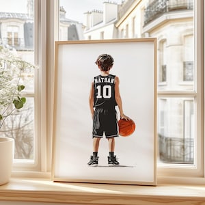 Könnte beinhalten: Eine gerahmte Illustration eines jungen Menschen, der ein schwarzes Basketballtrikot mit dem Namen "Nathan" und der Nummer "10" auf dem Rücken trägt. Die Person hält einen Basketball und blickt von der Kamera weg.
