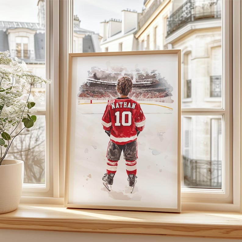 May include: A watercolor painting of a young hockey player wearing a red and white jersey with the name "Nathan" and the number "10" on the back. The player is standing on a snowy ice rink with a blurred background of a hockey stadium.