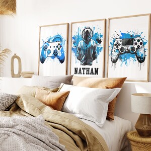 May include: Three framed prints with blue watercolor splashes and gamer-themed illustrations. The prints feature a video game controller, a hooded figure, and the name "NATHAN".