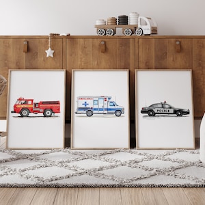 May include: Three framed watercolor prints of emergency vehicles: a red fire truck, a white and blue ambulance, and a black police car. The prints are displayed on a light gray rug in front of a wooden cabinet. A wooden toy train sits on top of the cabinet.