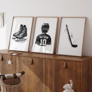 May include: Three black and white framed prints of hockey-themed illustrations. The first print shows a pair of hockey skates, the second print shows a hockey player wearing a jersey with the name "Nathan" and the number "10" on it, and the third print shows a hockey stick.