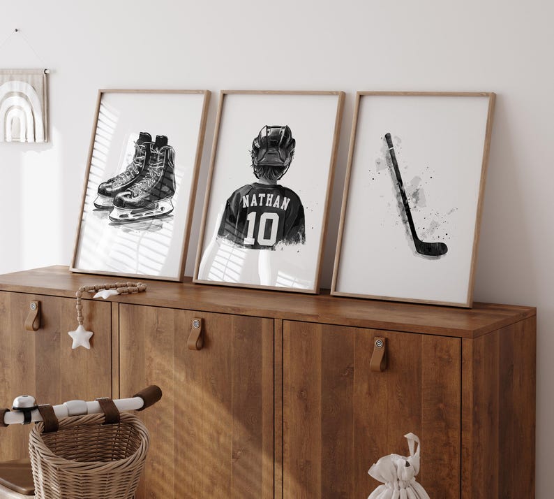 May include: Three black and white framed prints of hockey-themed illustrations. The first print shows a pair of hockey skates, the second print shows a hockey player wearing a jersey with the name "Nathan" and the number "10" on it, and the third print shows a hockey stick.