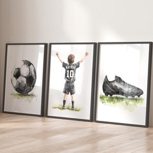 Peut inclure: Trois impressions encadr&eacute;es noires avec des illustrations &agrave; l'aquarelle d'un ballon de football, d'un gar&ccedil;on en uniforme de football avec le nom "Nathan" et le num&eacute;ro "10" au dos, et d'une chaussure de football noire.