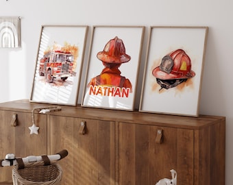 May include: Three framed watercolor prints featuring a fire truck, a firefighter's back with the name "NATHAN", and a firefighter's helmet. The prints have a warm color palette with red, orange, and brown tones, and are displayed on a wooden cabinet.
