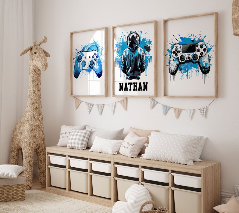 May include: Three framed prints with blue watercolor splashes and a gaming theme. The center print features a hooded figure with the name "NATHAN" below. The left and right prints feature a blue video game controller.
