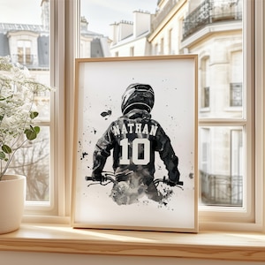 Peut inclure: Une impression encadr&eacute;e &agrave; l'aquarelle d'une personne &agrave; v&eacute;lo, vue de dos. La personne porte un casque et une veste avec le nom "NATHAN" et le num&eacute;ro "10" dans le dos. L'&oelig;uvre est dans des tons de gris et de noir.