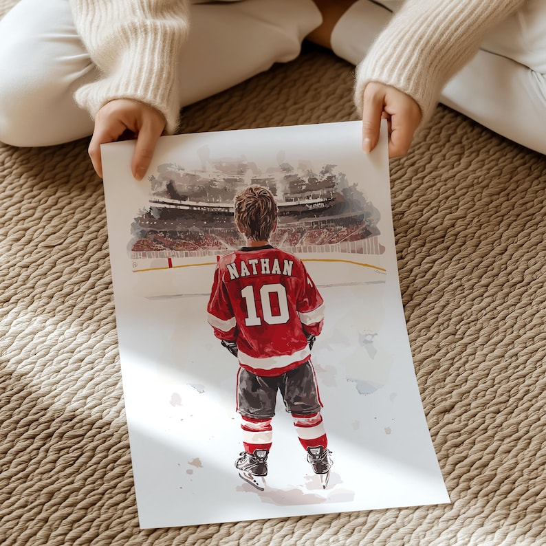 May include: A watercolor painting of a young hockey player wearing a red and white jersey with the name "Nathan" and the number "10" on the back. The player is standing on a hockey rink with a blurred background of a stadium.