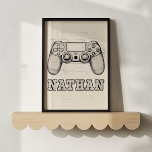 Könnte beinhalten: Ein gerahmter Druck mit einer detaillierten Skizze eines Gamecontrollers. Das Wort "NATHAN" ist in fetten Blockbuchstaben unter dem Controller aufgedruckt. Das Kunstwerk wird auf hellem Hintergrund gezeigt.