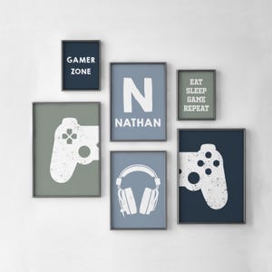 Könnte beinhalten: Eine Sammlung gerahmter Wandkunst mit Gaming-Motiven. Die Kunstwerke zeigen eine Controller-Grafik, Kopfhörer und Texte wie "Gamer Zone", "Eat Sleep Game Repeat" und "N Nathan". Die Farbpalette umfasst Blau-, Grün- und Weißtöne.