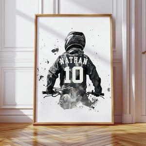 Peut inclure: Impression artistique encadr&eacute;e d'une personne &agrave; v&eacute;lo, portant un casque et un maillot. Le maillot affiche le nom "NATHAN" et le num&eacute;ro "10". L'&oelig;uvre est principalement en noir, blanc et gris, avec des &eacute;claboussures de peinture.
