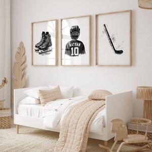 May include: Three black and white framed prints of hockey-themed artwork. The prints feature a hockey stick, a hockey player wearing a jersey with the name "Nathan" and the number "10", and a pair of hockey skates.