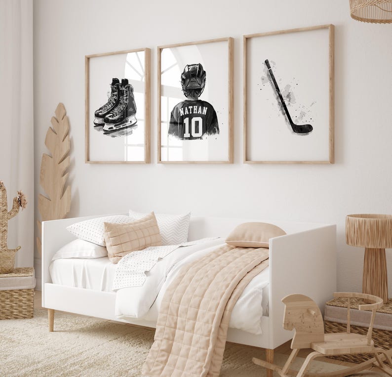 May include: Three black and white framed prints of hockey-themed artwork. The prints feature a hockey stick, a hockey player wearing a jersey with the name "Nathan" and the number "10", and a pair of hockey skates.