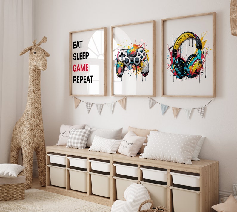 May include: Three framed prints with a gaming theme. The first print has the text "Eat Sleep Game Repeat" in black and red. The second print features a colorful illustration of a video game controller. The third print shows a pair of headphones with colorful paint splatters.