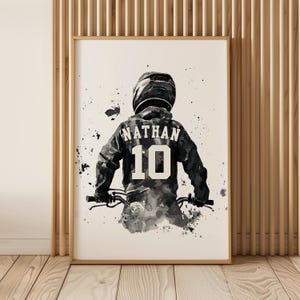 Peut inclure: Impression d'art encadr&eacute;e. Illustration &agrave; l'aquarelle en noir et blanc d'une personne &agrave; v&eacute;lo, vue de dos. Le maillot porte le nom "NATHAN" et le num&eacute;ro "10". L'&oelig;uvre utilise des nuances de gris et de noir, avec un casque.