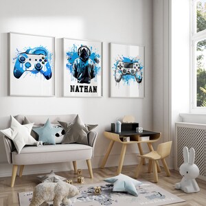 May include: Three framed prints with blue and white paint splatters. The center print features a black silhouette of a person wearing a hooded sweatshirt and headphones with the name "NATHAN" below. The prints on either side feature a white video game controller with blue paint splatters.