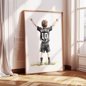 Peut inclure: Une peinture &agrave; l'aquarelle d'un jeune gar&ccedil;on portant un maillot de football noir avec le nom "Nathan" et le num&eacute;ro "10" au dos. Il l&egrave;ve les bras en l'air, c&eacute;l&eacute;brant un but.