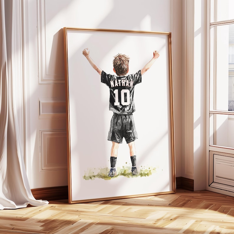 Peut inclure: Une peinture &agrave; l'aquarelle d'un jeune gar&ccedil;on portant un maillot de football noir avec le nom "Nathan" et le num&eacute;ro "10" au dos. Il l&egrave;ve les bras en l'air, c&eacute;l&eacute;brant un but.