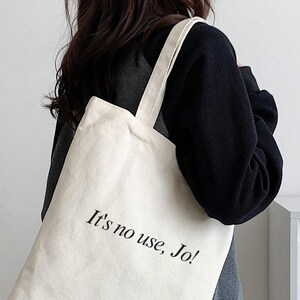 Pode incluir: Uma bolsa tote de lona branca com texto preto que diz "It's no use, Jo!"